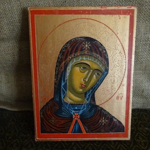May include: A vintage religious icon depicting the Virgin Mary with a gold halo and a blue and red robe. The icon is painted on a wooden panel with a red border.