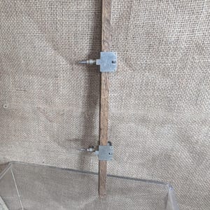 May include: A vintage wooden marking gauge with two adjustable metal pins. The gauge is made of a dark wood and has two metal pieces that slide along the wood. The background is a textured, neutral-coloured fabric.