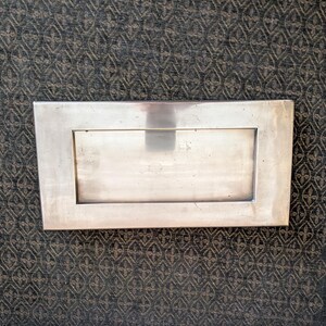 May include: A rectangular, silver-colored metal picture frame with a recessed center. The frame has a simple, clean design with a polished finish. The frame is likely designed to hold a photograph or artwork.