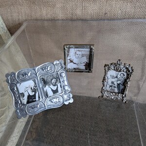 May include: Three antique silver picture frames of varying sizes, each holding a black and white photograph. The frames have ornate designs, with one holding two photos. The photos appear to be vintage portraits.