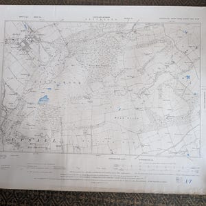 May include: A vintage map of the Cleveland area, featuring detailed topographical information. The map is printed on aged paper and held down by four coins. The map includes place names, roads, and contour lines, with a scale and grid system.