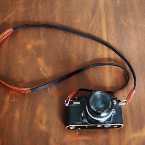 May include: A black camera with a brown leather strap. The camera has a silver lens and the word "YASHICA" is printed on the front.