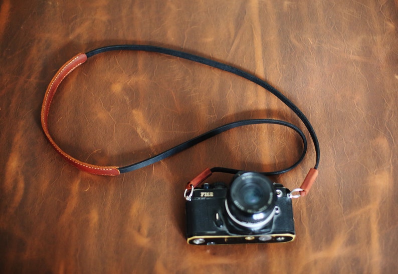 May include: A black camera with a brown leather strap. The camera has a silver lens and the word "YASHICA" is printed on the front.