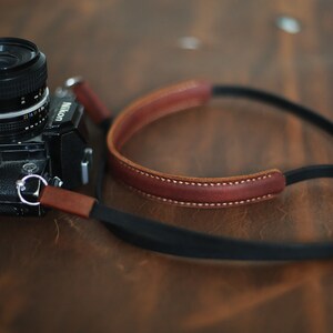 May include: A black Nikon camera with a brown leather camera strap. The camera has a silver ring around the lens.