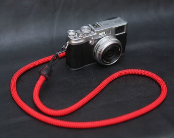 May include: A silver camera with a black lens and a red camera strap. The camera is on a black surface.