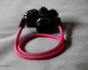 May include: A pink and blue camera strap with a black camera attached.