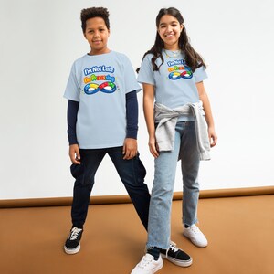 May include: Two children wearing light blue t-shirts with the text "I'm Not Late I'm Processing" and a colorful infinity symbol. The children are wearing dark blue pants and sneakers. The background is a solid brown.