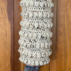Modern boho style grocery bag holder. It measures 15 inches in length.  Features bobble crochet stitches in rows around it. Bag saver is hand crocheted in a beige fleck color. Large hook for hanging anywhere you like. Goes well with farmhouse style.