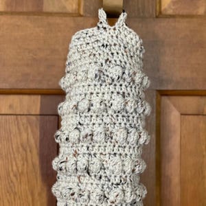 Modern boho style grocery bag holder. It measures 15 inches in length.  Features bobble crochet stitches in rows around it. Bag saver is hand crocheted in a beige fleck color. Large hook for hanging anywhere you like. Goes well with farmhouse style.
