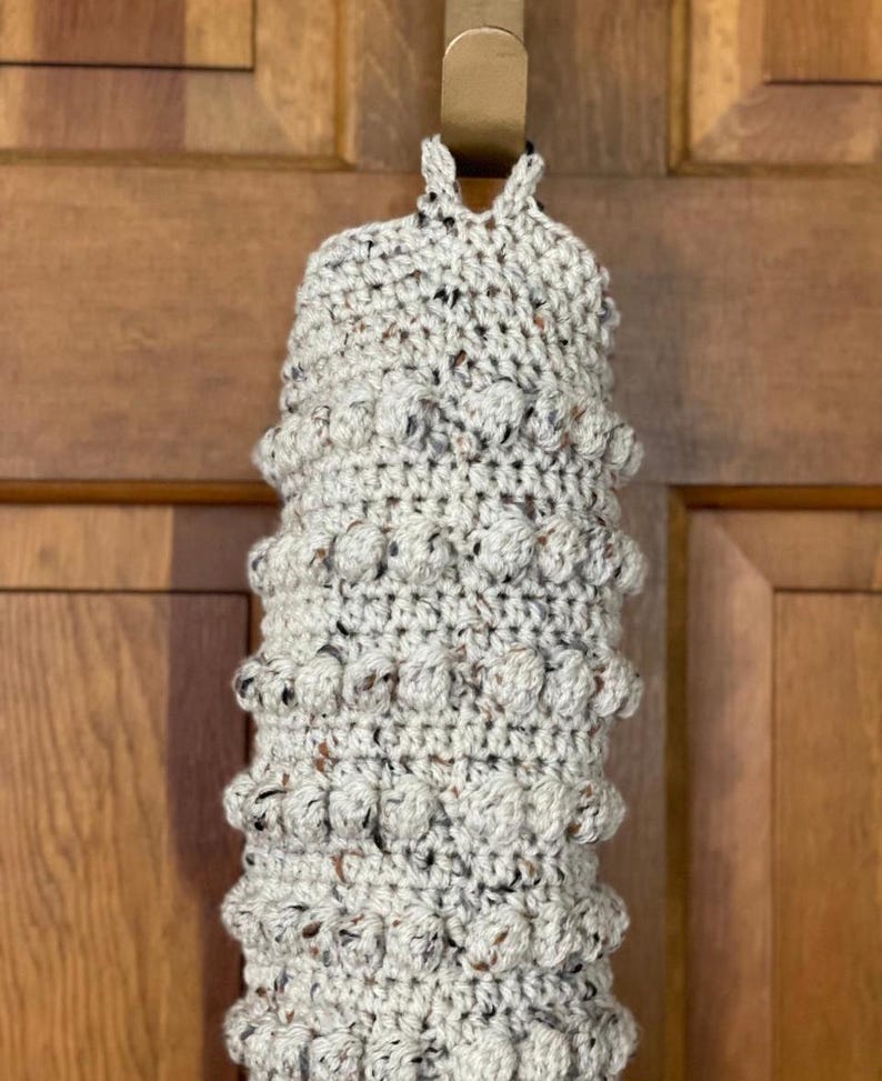 Modern boho style grocery bag holder. It measures 15 inches in length.  Features bobble crochet stitches in rows around it. Bag saver is hand crocheted in a beige fleck color. Large hook for hanging anywhere you like. Goes well with farmhouse style.