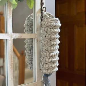 Modern boho style grocery bag holder. It measures 15 inches in length.  Features bobble crochet stitches in rows around it. Bag saver is hand crocheted in a beige fleck color. Large hook for hanging anywhere you like. Goes well with farmhouse style.