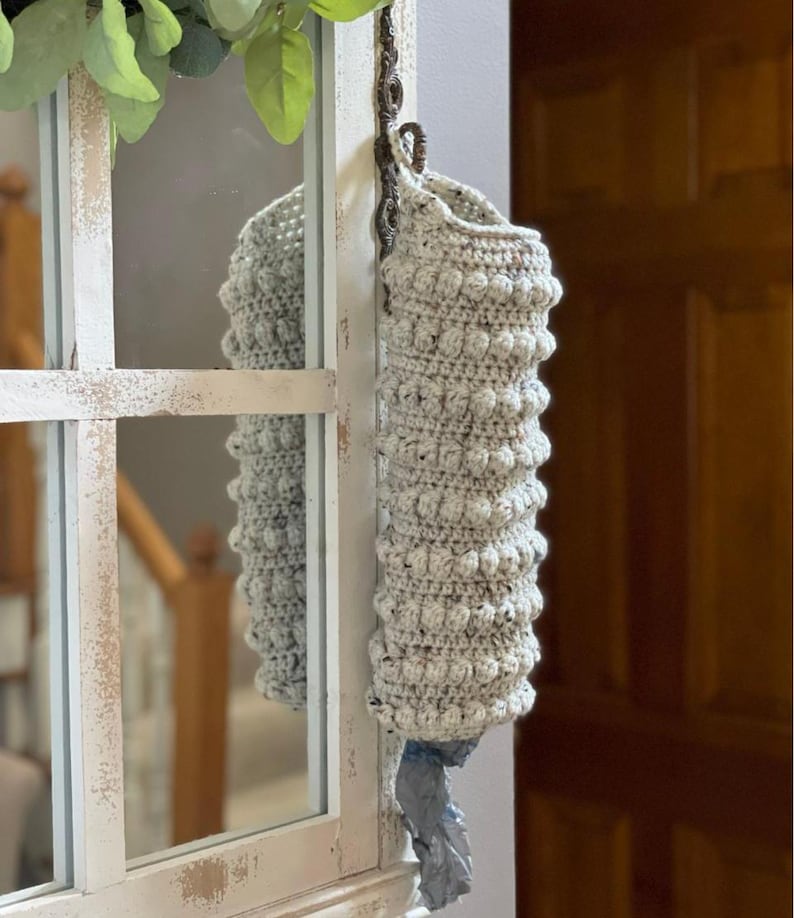 Modern boho style grocery bag holder. It measures 15 inches in length.  Features bobble crochet stitches in rows around it. Bag saver is hand crocheted in a beige fleck color. Large hook for hanging anywhere you like. Goes well with farmhouse style.