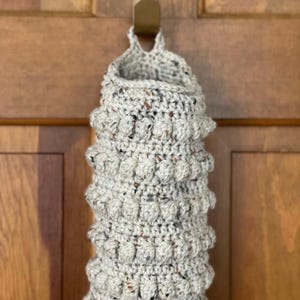 Modern boho style grocery bag holder. It measures 15 inches in length.  Features bobble crochet stitches in rows around it. Bag saver is hand crocheted in a beige fleck color. Large hook for hanging anywhere you like. Goes well with farmhouse style.