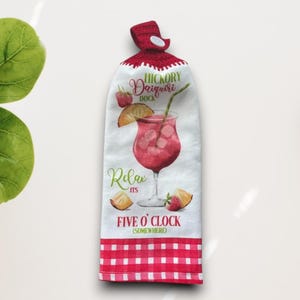May include: A white kitchen towel with a red and white checkered bottom and a red crocheted top. The towel features a watercolor illustration of a cocktail with the text "Hickory Daiquiri Dock" and "Relax its Five O'Clock (Somewhere)".