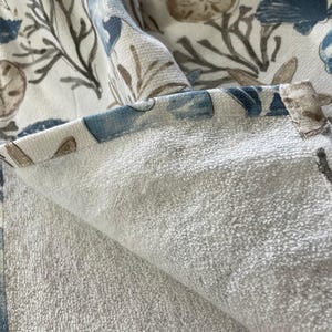 A close-up of the folded edge of a white terry cloth hand towel, revealing the soft texture and the patterned fabric on the reverse side.