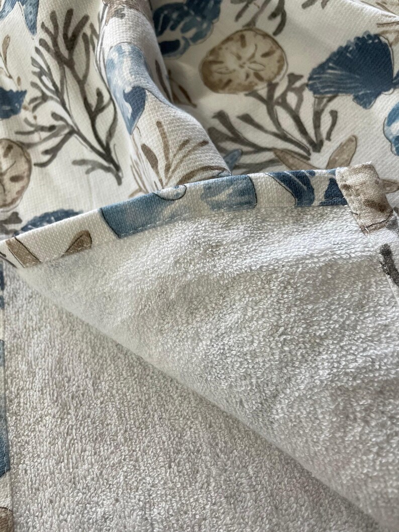 A close-up of the folded edge of a white terry cloth hand towel, revealing the soft texture and the patterned fabric on the reverse side.