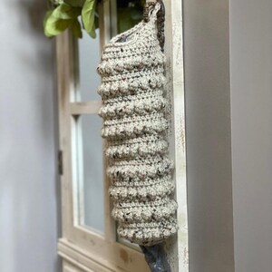 Modern boho style grocery bag holder. It measures 15 inches in length.  Features bobble crochet stitches in rows around it. Bag saver is hand crocheted in a beige fleck color. Large hook for hanging anywhere you like. Goes well with farmhouse style.