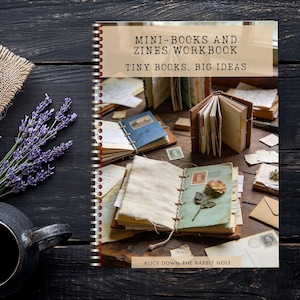 May include: A spiral-bound workbook titled MINI-BOOKS AND ZINES WORKBOOK: TINY BOOKS, BIG IDEAS by ALICE DOWN: THE RABBIT HOLE. The cover features a photograph of several small handmade books, loose papers, stamps, and a dried flower on a wooden surface.