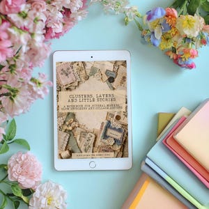 May include: A white tablet displaying a digital book cover titled Clusters, Layers and Little Stories: A Workbook for Journal Makers, Slow Stitchers and Collage Artists by Alice Down the Rabbit Hole, surrounded by pink and multicoloured flowers.