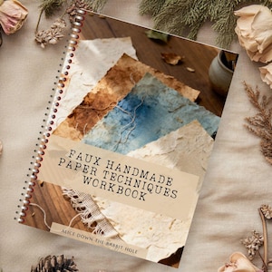 May include: A spiral-bound workbook titled FAUX HANDMADE PAPER TECHNIQUES WORKBOOK with a subtitle ALICE DOWN THE RABBIT HOLE. The cover features a collage of textured paper in shades of brown, blue, and cream, with a visible wire binding on the left side.