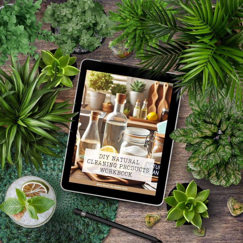 Op de afbeelding: Een digitale tablet met een werkboek met de titel "DIY Natural Cleaning Products Workbook" met een groene achtergrond en een foto van een keukenblad met schoonmaakmiddelen. De tablet is omringd door groene planten op een houten oppervlak.