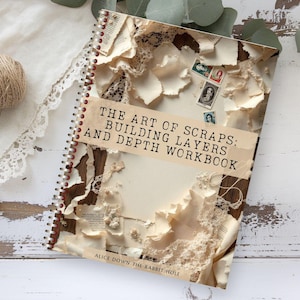 Può includere: Un quaderno a spirale intitolato "THE ART OF SCRAPS: BUILDING LAYERS AND DEPTH WORKBOOK" con una copertina a collage di carta strappata, pizzo e francobolli vintage. Un gomitolo di spago e finiture in pizzo sono sullo sfondo.