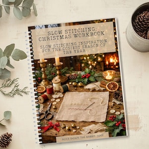 Könnte beinhalten: Ein spiralgebundenes Arbeitsbuch mit dem Titel SLOW STITCHING: CHRISTMAS WORKBOOK, SLOW STITCHING INSPIRATION FOR THE COSIEST SEASON OF THE YEAR von ALICE DOWN THE RABBIT HOLE. Das Cover zeigt eine festliche Szene mit Stoff, Nadeln und Dekoration.