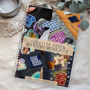 Puede incluir: Un cuaderno con espiral titulado "Creative Patch Mending Workbook" con varios parches de tela. Los parches son de diferentes colores y patrones, incluyendo diseños de mezclilla, cuadros y florales. El libro está sobre una superficie de color neutro.