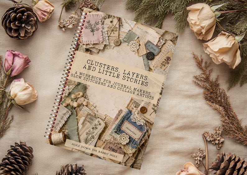 May include: A spiral-bound workbook titled Clusters, Layers and Little Stories: A Workbook for Journal Makers, Slow Stitchers and Collage Artists by Alice Down the Rabbit Hole, featuring a collage cover with fabric scraps, buttons, and paper.