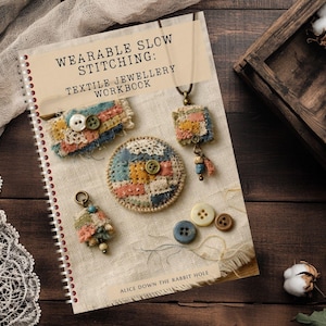 May include: A spiral-bound workbook titled Wearable Slow Stitching: Textile Jewellery Workbook by Alice Down The Rabbit Hole. The cover features images of handmade fabric jewelry, including a rectangular patch, a circular brooch, and a pendant.