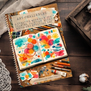 Puede incluir: Un cuaderno de ejercicios con espiral titulado ART CHALLENGES: A CREATIVE WORKBOOK FOR DRAWING, PAINTING, MIXED MEDIA AND EVERYDAY ART. La portada muestra un cuaderno abierto con círculos de acuarela coloridos, formas y materiales de arte.