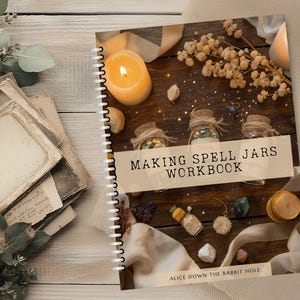 Pode incluir: Um caderno espiralado intitulado "Making Spell Jars Workbook" com uma estética rústica. A capa apresenta uma vela acesa, pequenos frascos e elementos decorativos sobre uma superfície de madeira. O texto na parte inferior diz "Alice Down The Rabbit Hole."