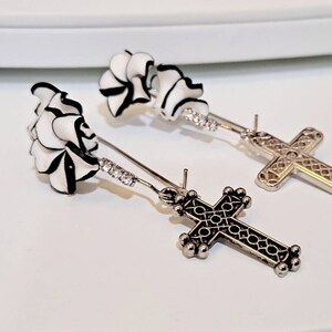 May include: A pair of silver earrings with a black and white flower design and a silver cross charm.