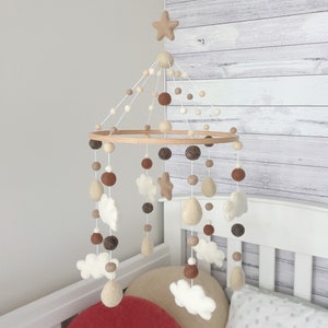 May include: A wooden baby mobile with felt clouds, stars, and raindrops hanging from a circular wooden frame. The mobile is decorated with brown, beige, and white felt balls.