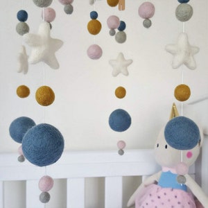 May include: A baby mobile with felt stars, balls, and a unicorn. The mobile features blue, pink, gray, and yellow felt balls. The stars are white and the unicorn is white with blue and pink accents.