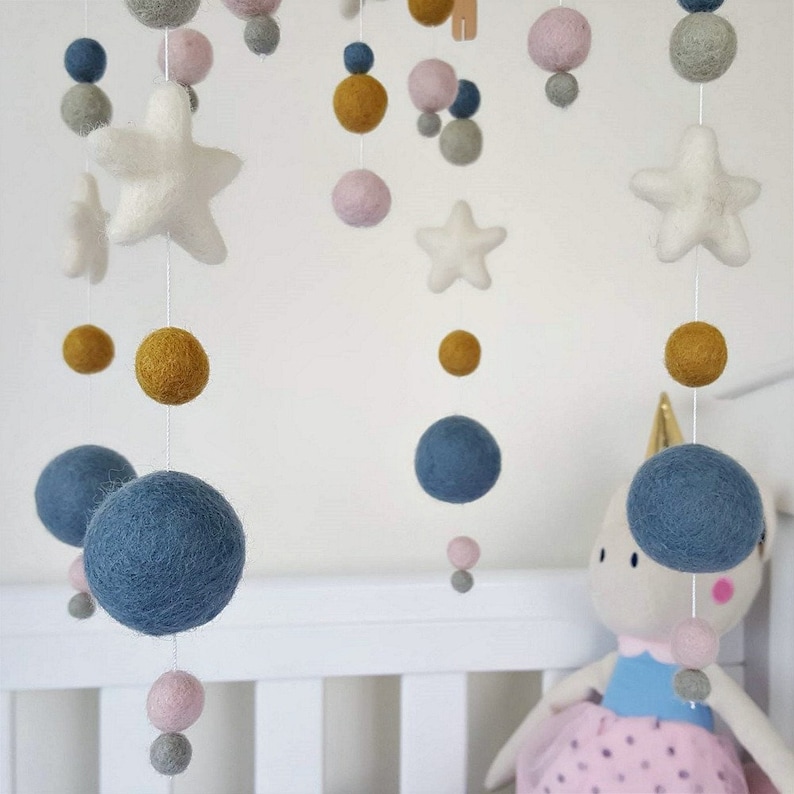 May include: A baby mobile with felt stars, balls, and a unicorn. The mobile features blue, pink, gray, and yellow felt balls. The stars are white and the unicorn is white with blue and pink accents.