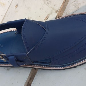 May include: A pair of blue leather sandals with a strap and buckle. The sandals have a decorative stitching pattern and a brown trim around the edge.