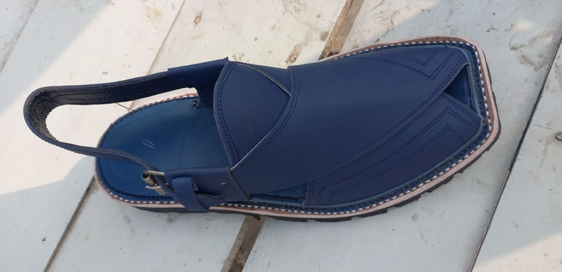 May include: A pair of blue leather sandals with a strap and buckle. The sandals have a decorative stitching pattern and a brown trim around the edge.