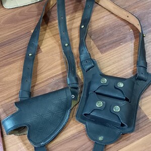 Puede incluir: Un holster de cuero negro con dos fundas para cargadores y una correa para el hombro. El holster tiene un patrón geométrico y detalles en latón.
