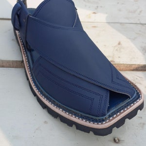 May include: A pair of dark blue leather sandals with a closed toe and an open heel. The sandals have a stitched design and a black rubber sole.