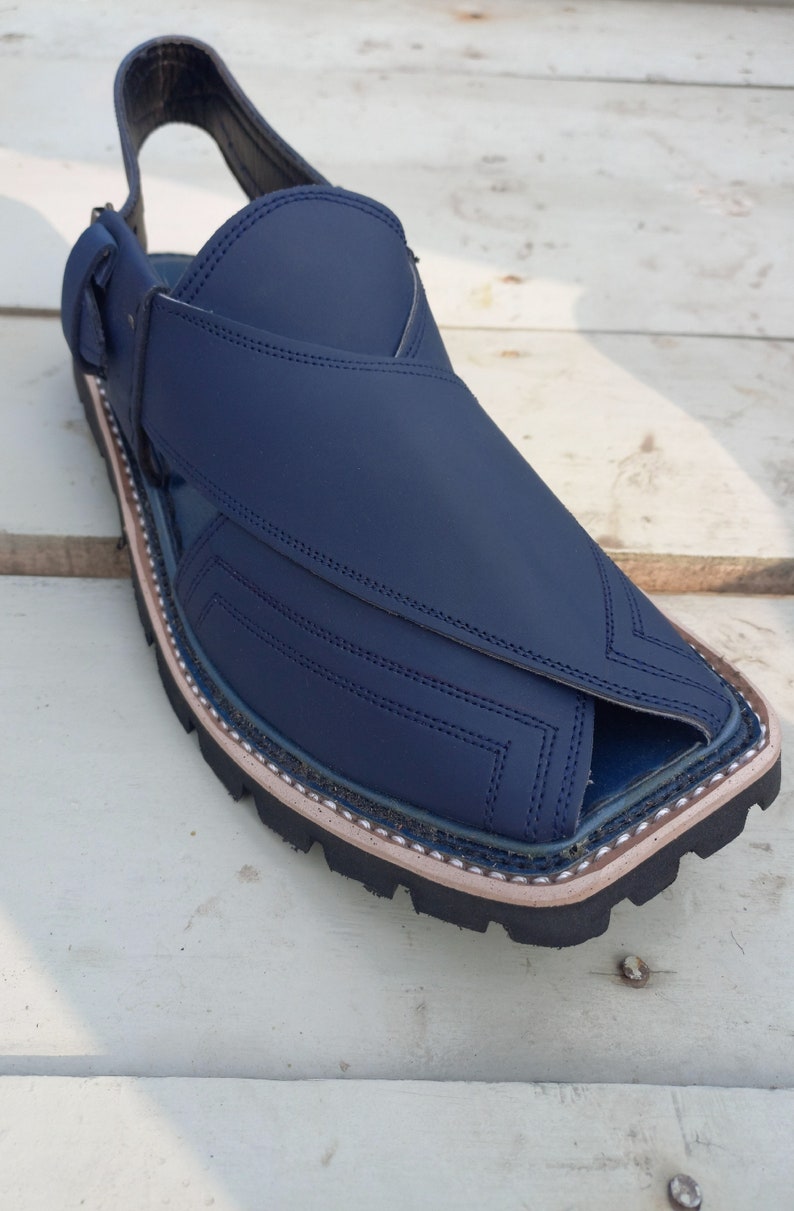 May include: A pair of dark blue leather sandals with a closed toe and an open heel. The sandals have a stitched design and a black rubber sole.