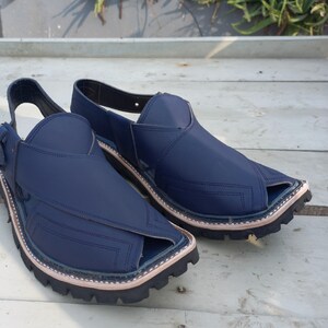 May include: A pair of dark blue leather sandals with a pointed toe and a strap across the top of the foot. The sandals have a thick, black rubber sole.