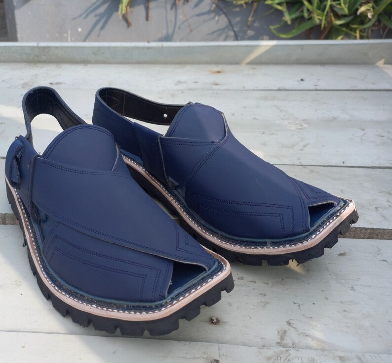 May include: A pair of dark blue leather sandals with a pointed toe and a strap across the top of the foot. The sandals have a thick, black rubber sole.