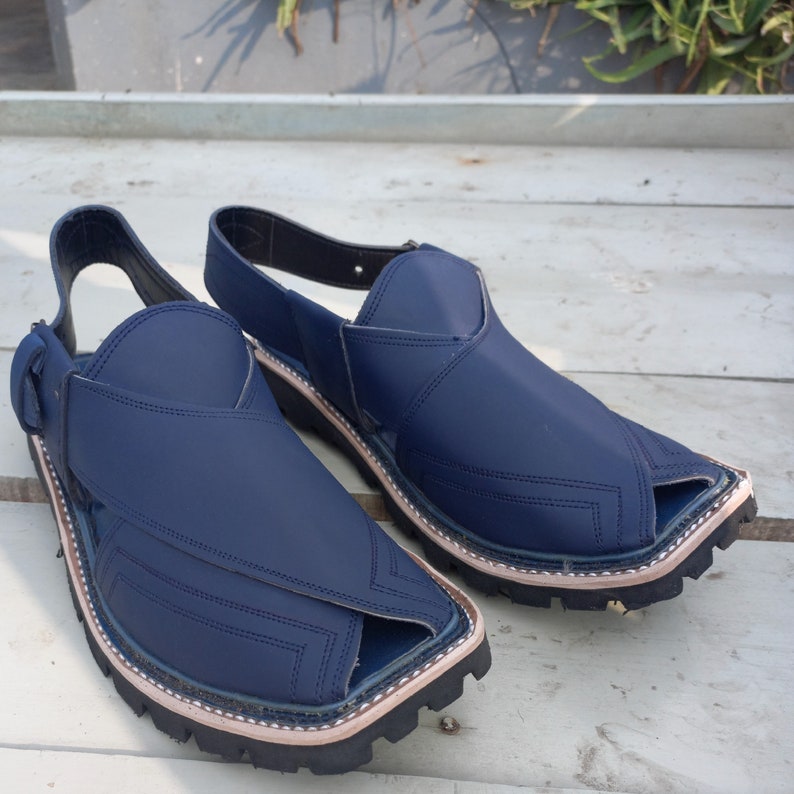 May include: A pair of dark blue leather sandals with a pointed toe and a strap across the top of the foot. The sandals have a stitched design and a thick rubber sole.