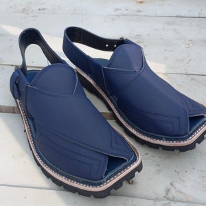 May include: A pair of dark blue leather sandals with a pointed toe and a strap around the ankle. The sandals have a stitched design and a thick rubber sole.