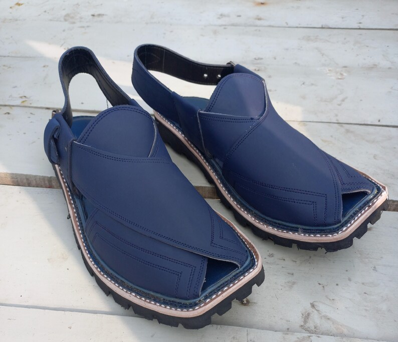 May include: A pair of dark blue leather sandals with a pointed toe and a strap around the ankle. The sandals have a stitched design and a thick rubber sole.