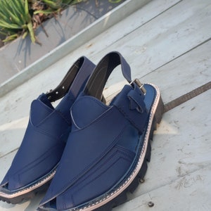 May include: A pair of dark blue leather sandals with a buckle strap and a thick black sole.