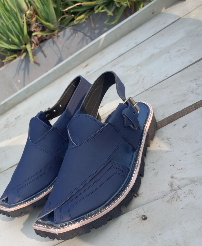 May include: A pair of dark blue leather sandals with a buckle strap and a thick black sole.