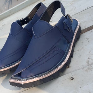 May include: A pair of dark blue leather sandals with a strap and buckle. The sandals have a thick, black sole with a light brown trim.