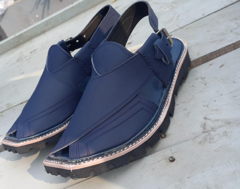 May include: A pair of dark blue leather sandals with a strap and buckle. The sandals have a thick, black sole with a light brown trim.